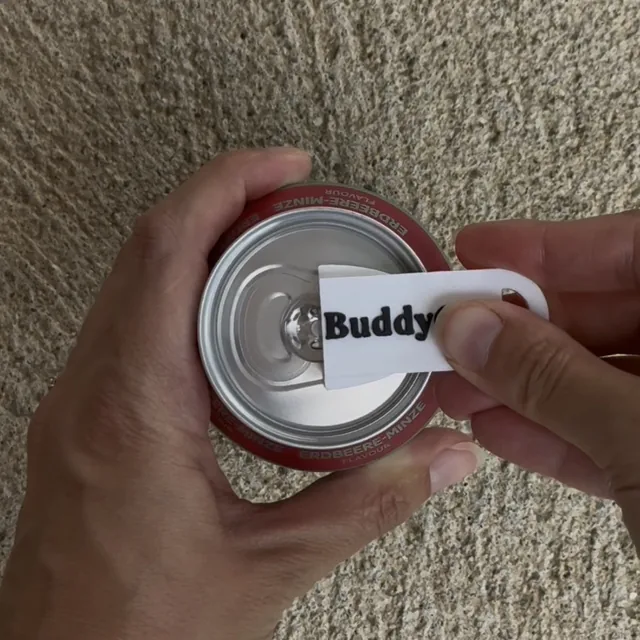 Une main tient une canette pendant que l’autre glisse le BuddyCan sous la languette, jusqu’à la butée.